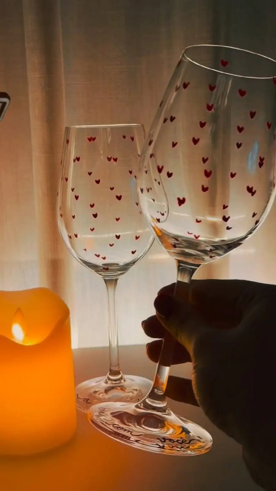Duas taças de vinho com corações pintados, contra a luz de uma vela